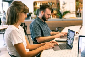 Two people working on laptops at a table in a cafe