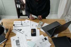 Person counting bills at a desk with a calculator and laptop