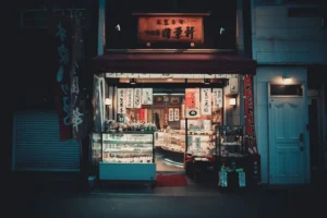 Small shop at night with hanging banners and a lit sign