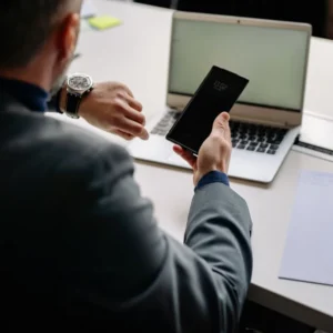 Man checking his watch while holding a phone showing the time